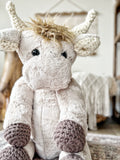 Plush toy highland cow with tan fur and crochet horns, ears, and feet.