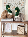 Two plush duck toys on a wooden table with floral wallpaper in the background