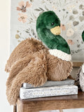 Plush duck toy on top of books with a floral wallpaper background