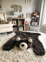A large brown bear rug on a cream colored carpet in a woodland themed bedroom. The bear rug is made by ClaraLoo with plush faux fur. The animal rug has cream colored ears and face with a black nose.